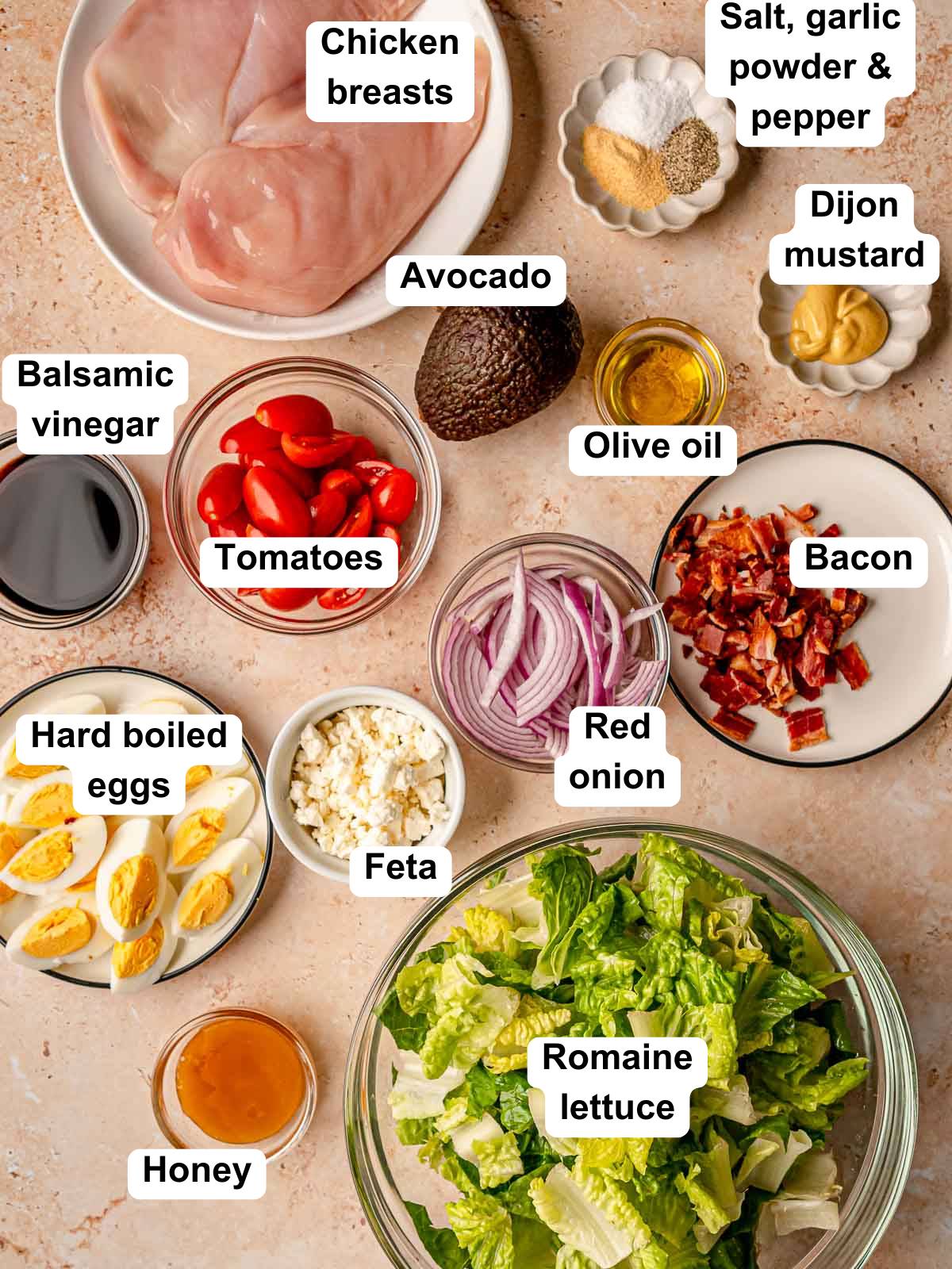 Labeled ingredients for chicken Cobb salad including romaine, chicken, avocado, bacon, eggs, tomatoes, and feta.