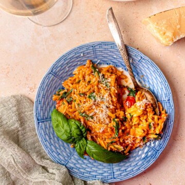 Tomato vodka orzo with spinach and parmesan served on a blue plate with fresh basil.