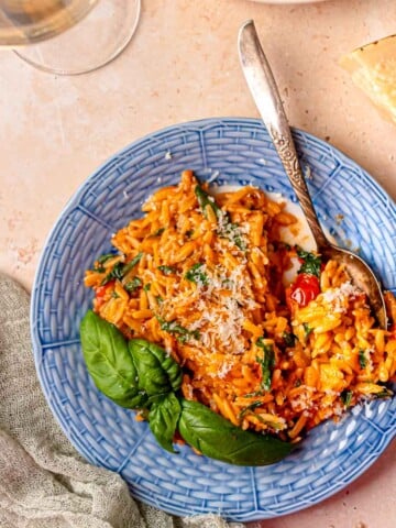 Tomato vodka orzo with spinach and parmesan served on a blue plate with fresh basil.