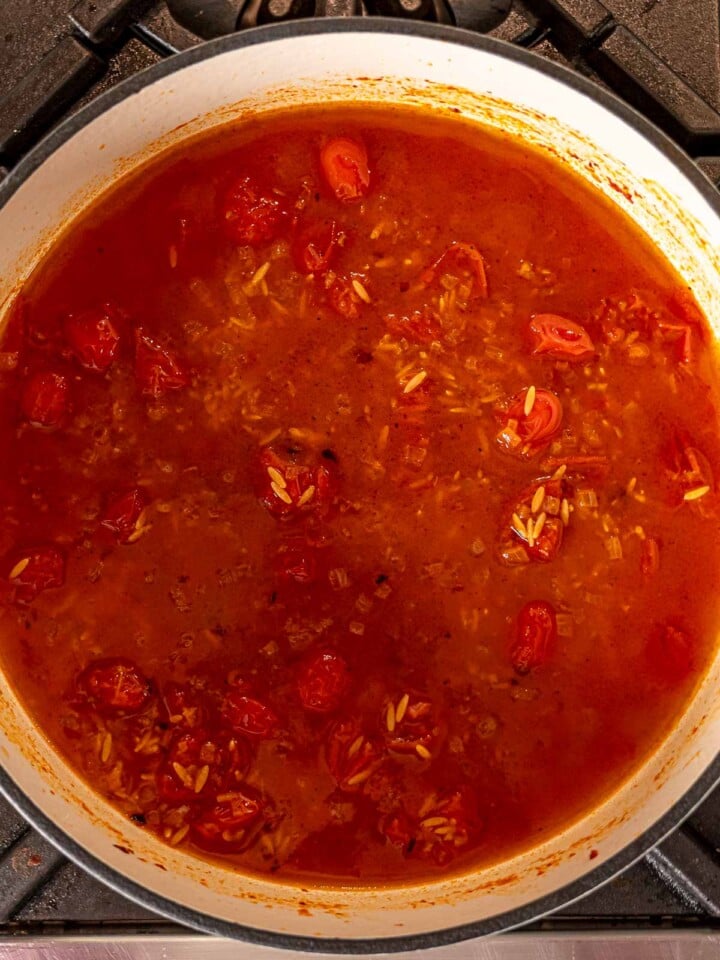 Orzo simmering in tomato vodka sauce with visible cherry tomatoes.