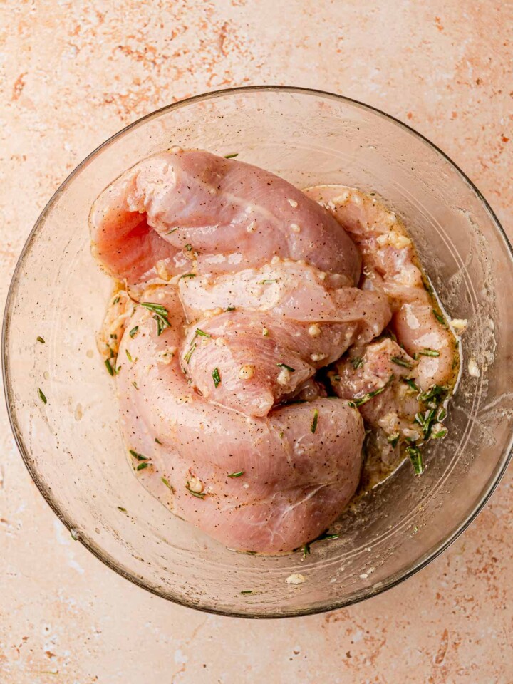 Raw, marinated chicken breasts placed on a grill, beginning to cook over direct heat.