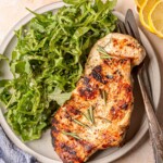 Grilled chicken breast with rosemary served next to a large portion of arugula salad.