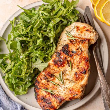 Grilled chicken breast with rosemary served next to a large portion of arugula salad.