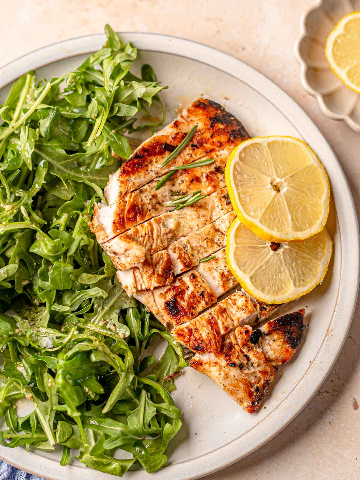 Sliced grilled chicken breast served with lemon slices and arugula salad.
