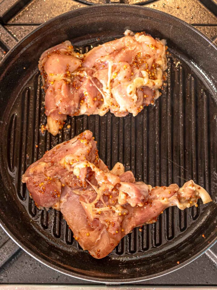 Chicken thighs cooking on a stovetop grill pan with visible mustard marinade.