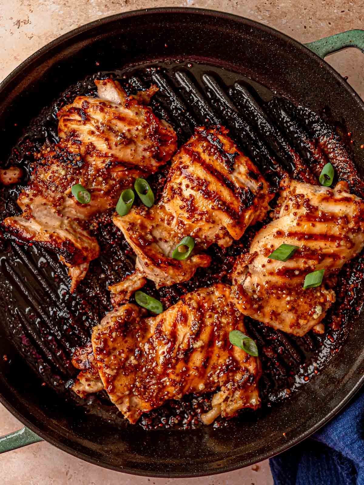Grilled chicken thighs with honey mustard glaze and grill marks in a cast iron pan.