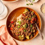 Teriyaki ground beef served with rice, broccoli, red peppers, and scallions in a brown bowl.