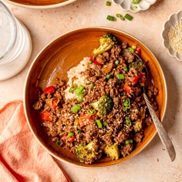 Teriyaki ground beef served with rice, broccoli, red peppers, and scallions in a brown bowl.