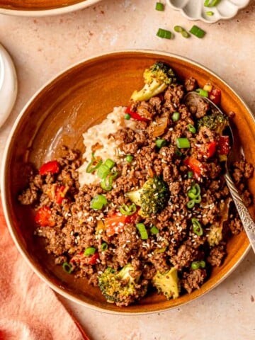 Teriyaki ground beef served with rice, broccoli, red peppers, and scallions in a brown bowl.