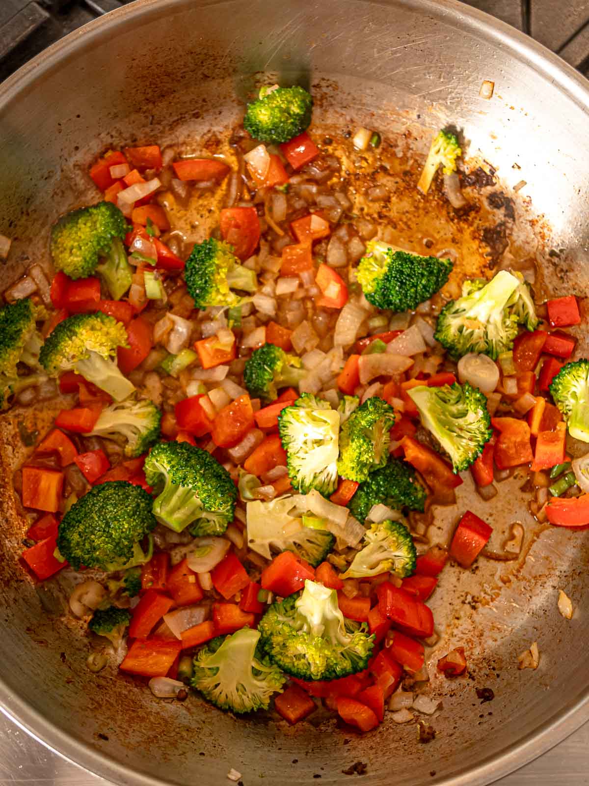 Broccoli and red peppers sautéing in a skillet with onion and garlic.