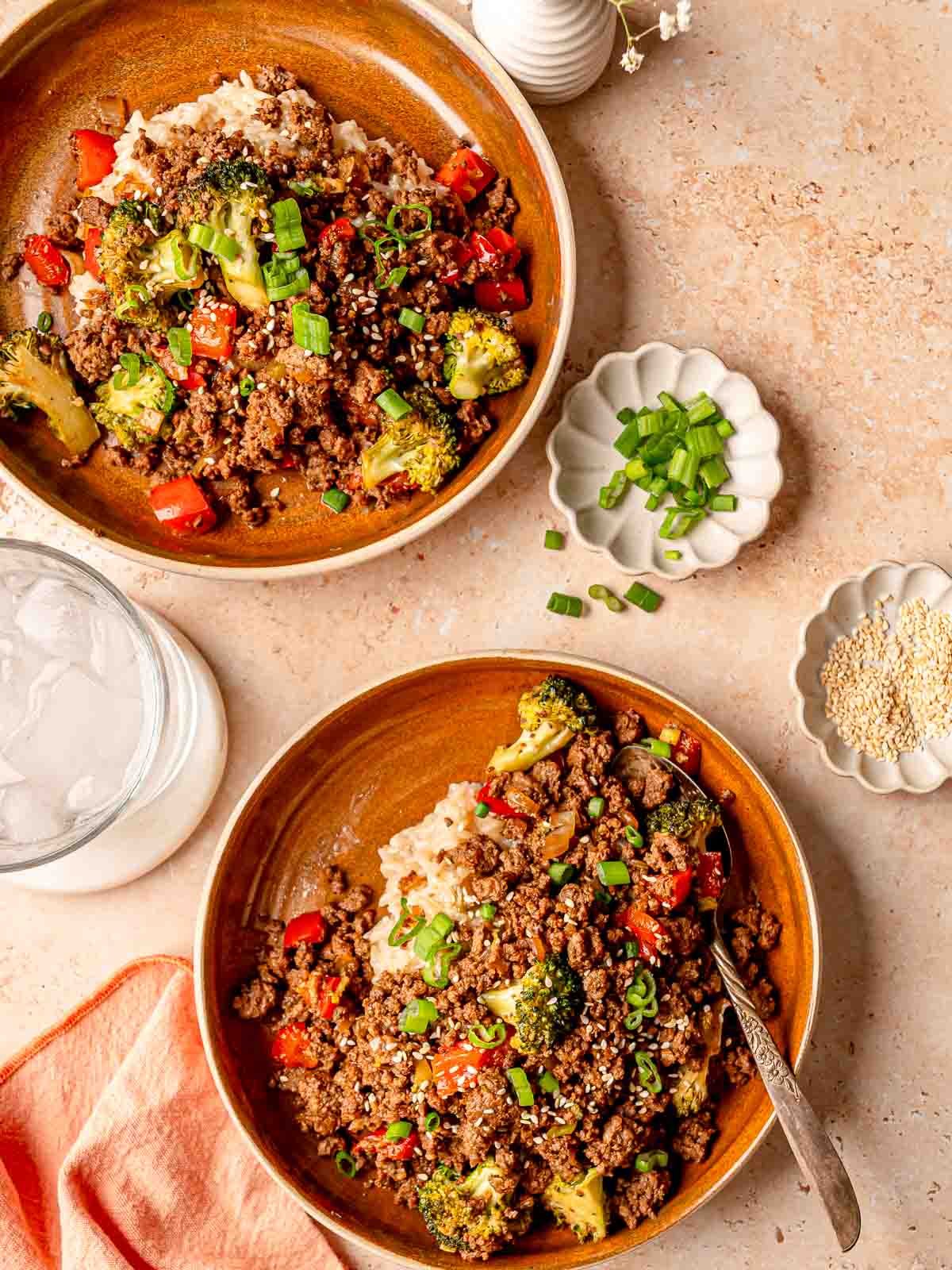 Two bowls of teriyaki beef and vegetables with rice, garnished with scallions and sesame seeds.