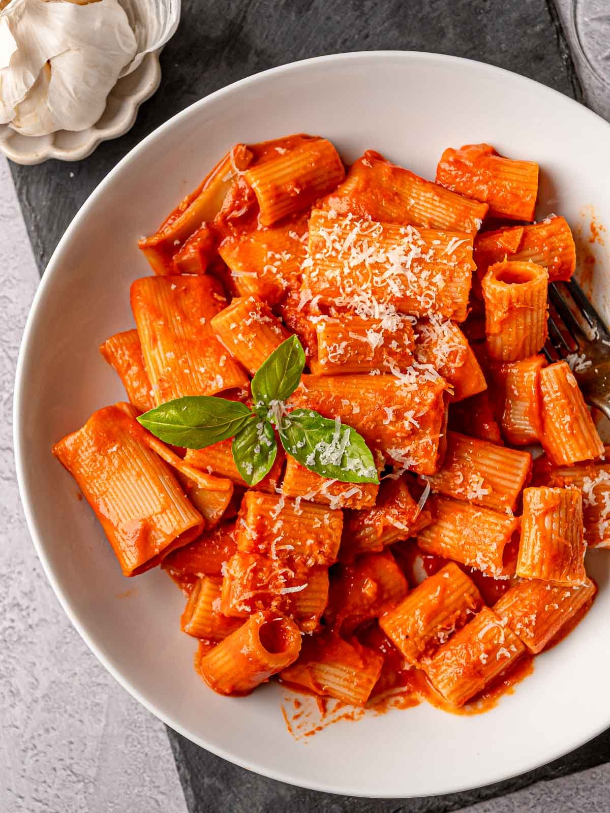 Rigatoni pasta tossed in a creamy pink tomato sauce, garnished with grated cheese and fresh basil, served in a white bowl.