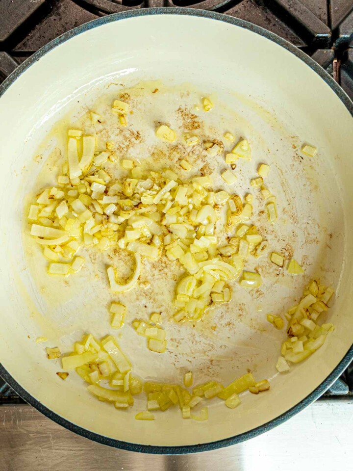 Chopped onions sizzling in olive oil in a white Dutch oven as the base for buffalo chicken pasta.
