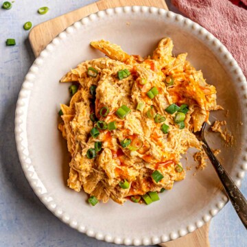 A bowl of creamy buffalo chicken pasta garnished with fresh green onions and buffalo sauce drizzle.