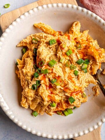 A bowl of creamy buffalo chicken pasta garnished with fresh green onions and buffalo sauce drizzle.