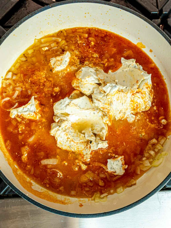 Buffalo sauce and cream cheese melting together with onions in a Dutch oven.