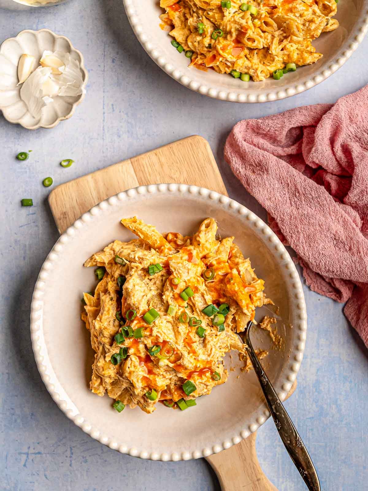 Creamy buffalo chicken pasta served in bowls, garnished with sliced green onions and drizzled with buffalo sauce.