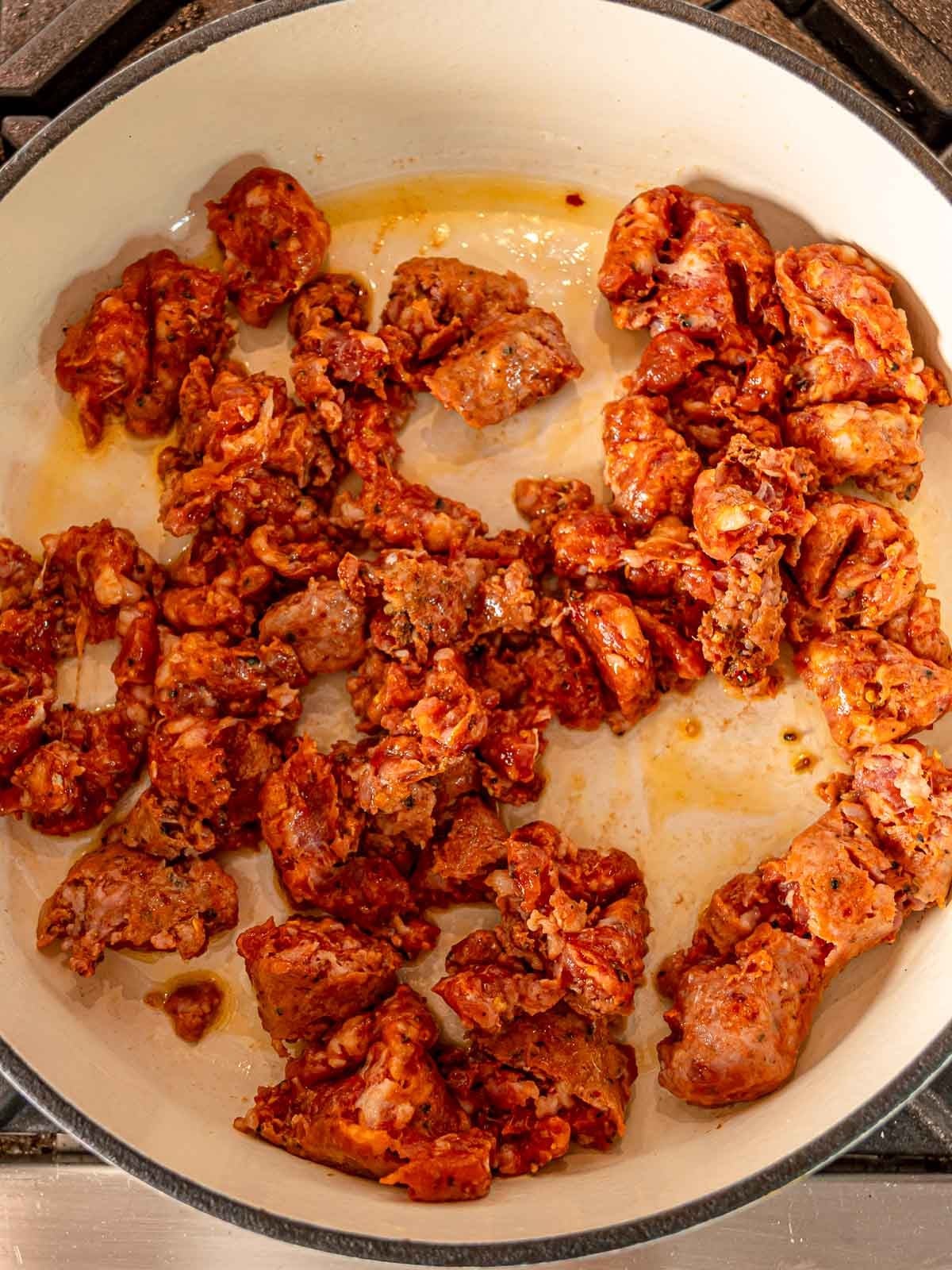 Italian sausage cooking in a Dutch oven until browned, the first step in making sausage and peppers pasta.