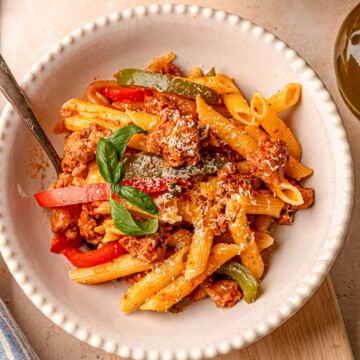 Bowl of sausage and peppers pasta topped with Parmesan and basil, ready to serve.