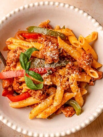 Bowl of sausage and peppers pasta topped with Parmesan and basil, ready to serve.