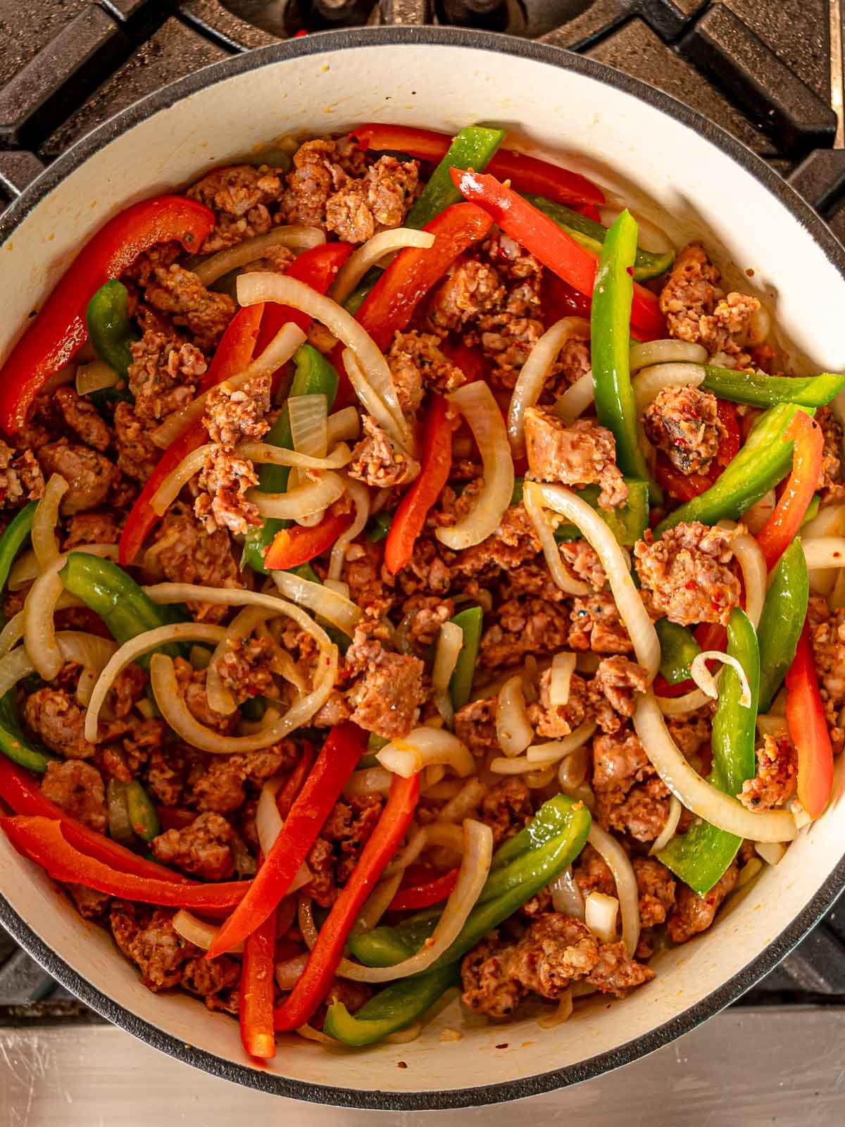 Sliced red and green bell peppers and onions sautéed with cooked sausage in a large pot.