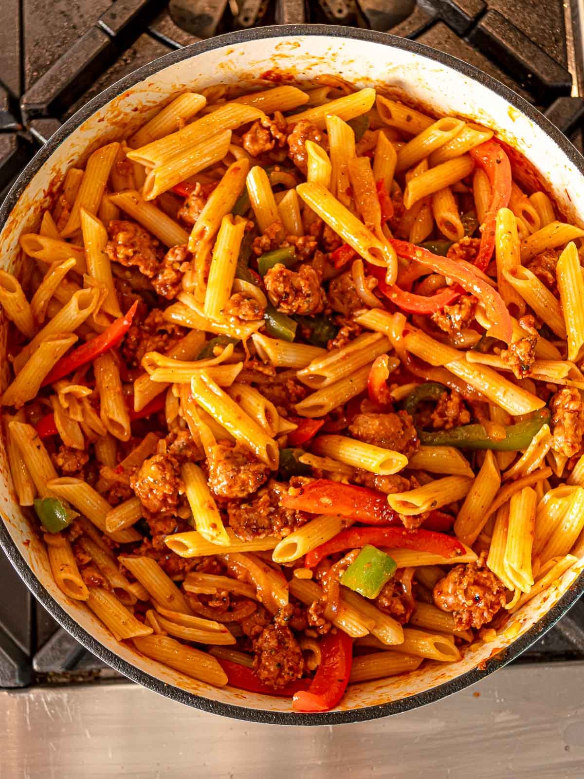 Cooked penne pasta mixed into the sausage and pepper marinara sauce in a large pot.