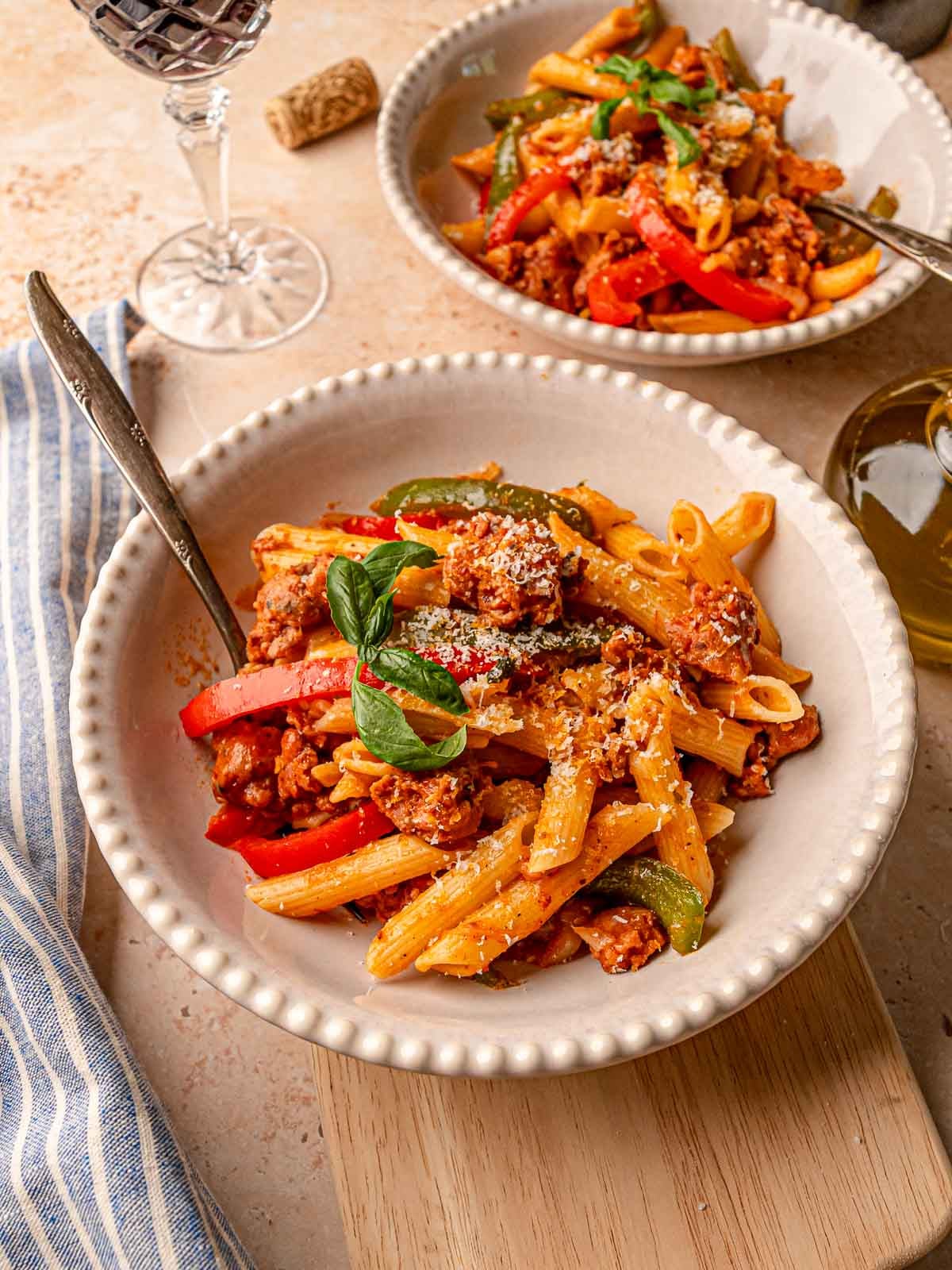 Sausage and peppers pasta in a white bowl with visible red and green bell peppers.