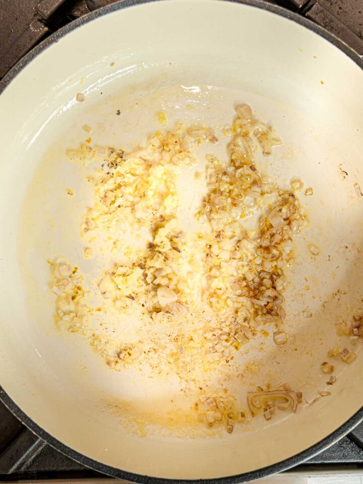 Chopped shallots and garlic sautéing in vegan butter in a Dutch oven.