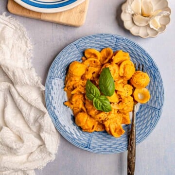 Orecchiette pasta in a creamy pumpkin sauce topped with basil, served on a blue plate with fork.