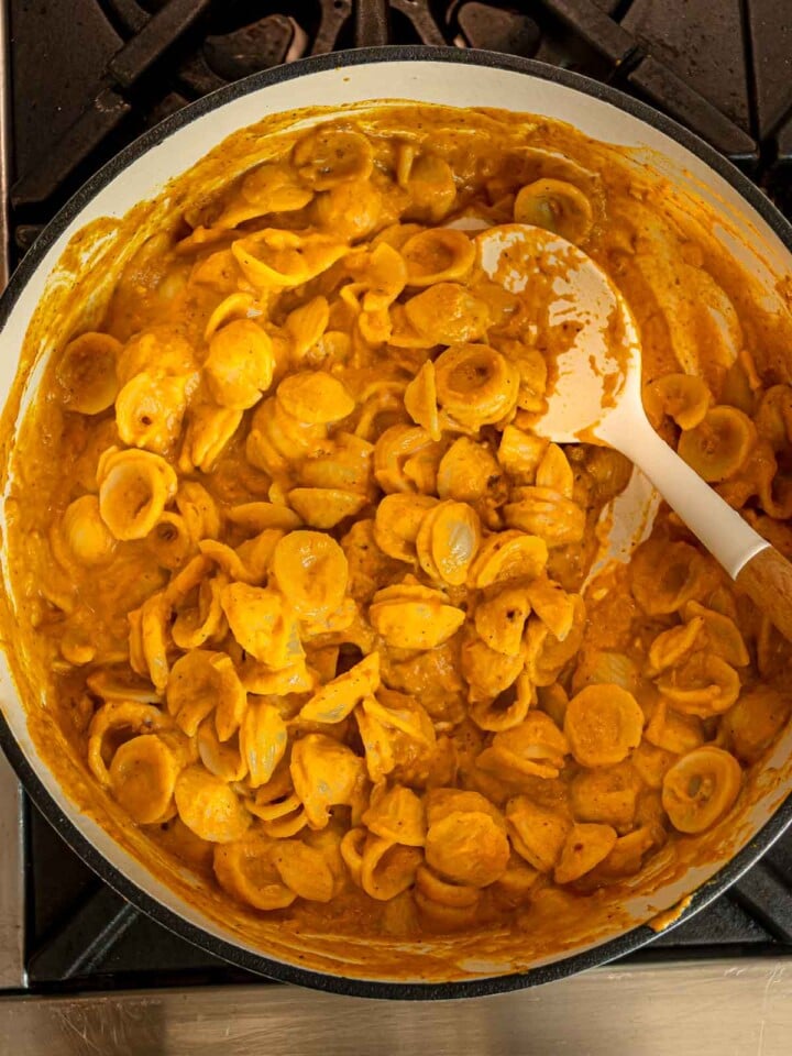 Orecchiette pasta stirred into creamy pumpkin sauce with a white spoon.