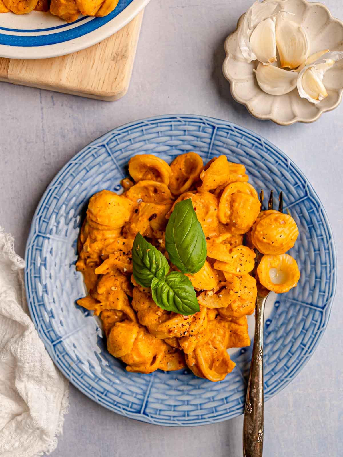 Orecchiette pasta coated in creamy pumpkin sauce, garnished with fresh basil, served on a textured blue plate.
