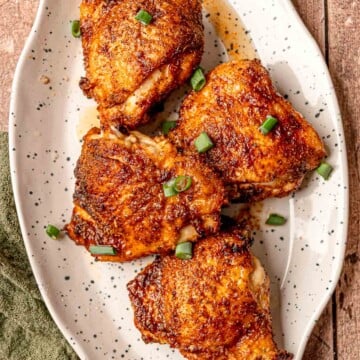 Four air-fried chicken thighs with a crisp dry rub exterior, plated on a speckled white serving dish.