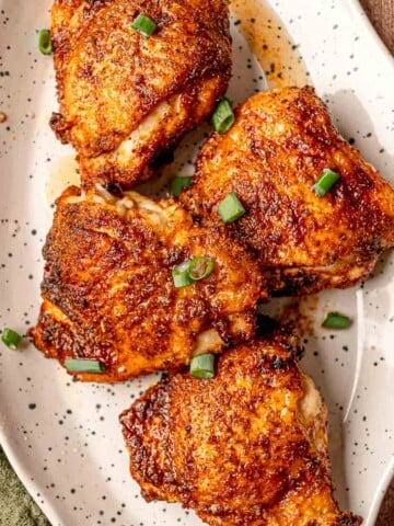 Four air-fried chicken thighs with a crisp dry rub exterior, plated on a speckled white serving dish.