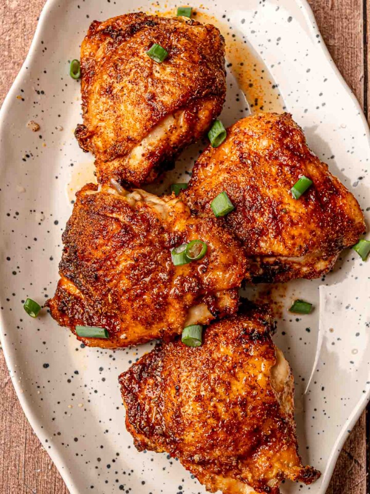 Crispy air fryer chicken thighs with browned, flavorful skin, garnished with fresh scallions on a serving platter.