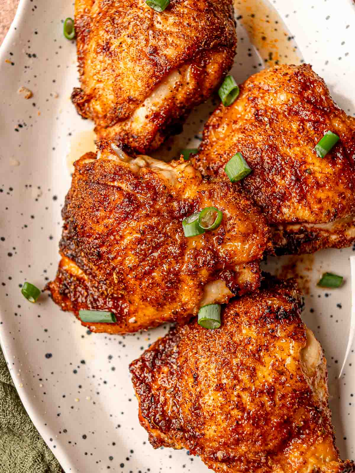 Crispy, browned chicken thighs fresh from the air fryer on a speckled platter, topped with chopped green onions.