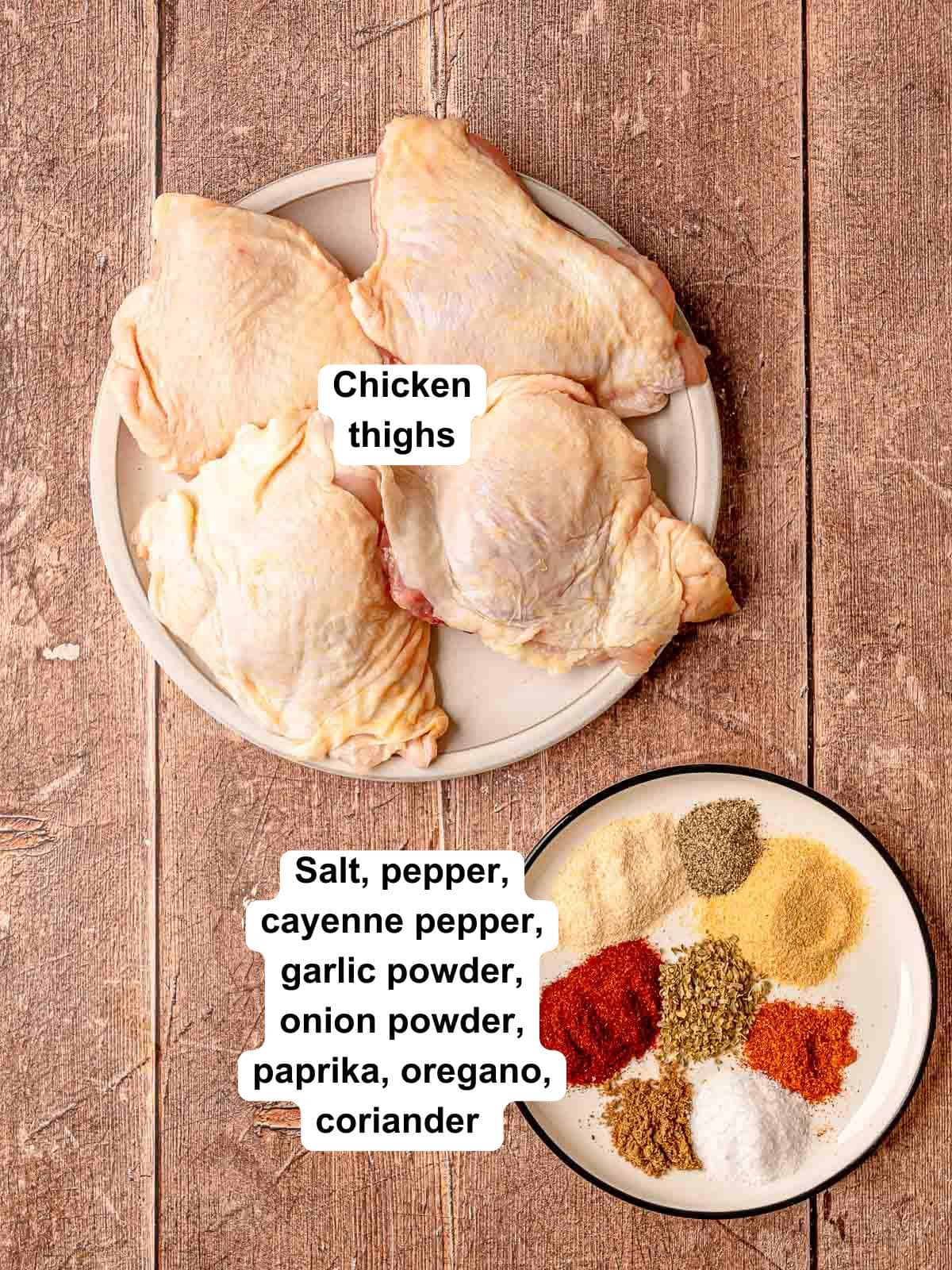 Raw chicken thighs on a plate beside a dish of colorful spices including paprika, garlic powder, cayenne, oregano, coriander, and salt.