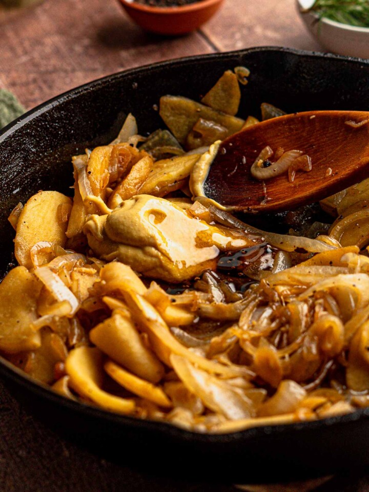 Sliced apples and caramelized onions sautéing with Dijon mustard and seasonings in a cast iron pan.