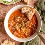 A bowl of slow cooker beef and barley soup served with crusty bread and fresh thyme.