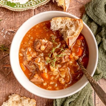 A bowl of slow cooker beef and barley soup served with crusty bread and fresh thyme.