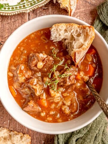 A bowl of slow cooker beef and barley soup served with crusty bread and fresh thyme.