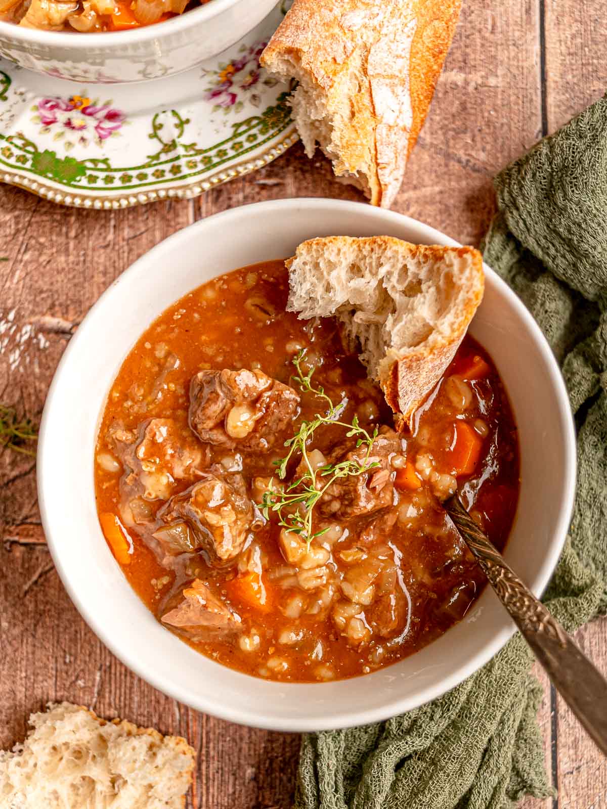 Beef and barley soup with chunks of beef, vegetables, and barley served with bread.