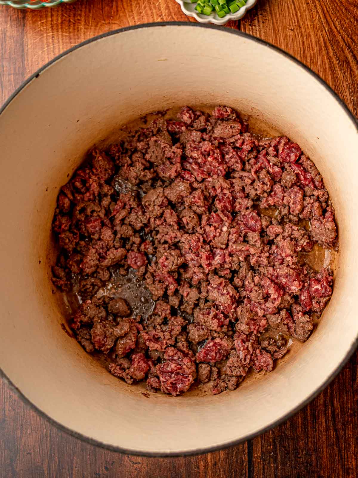 Crumbled ground beef browning in a large Dutch oven on a wooden surface.