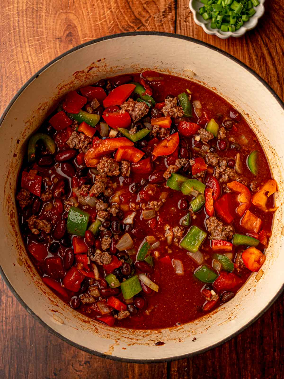 Colorful chili mixture of beef, beans, tomatoes, onions, and bell peppers simmering together in a Dutch oven