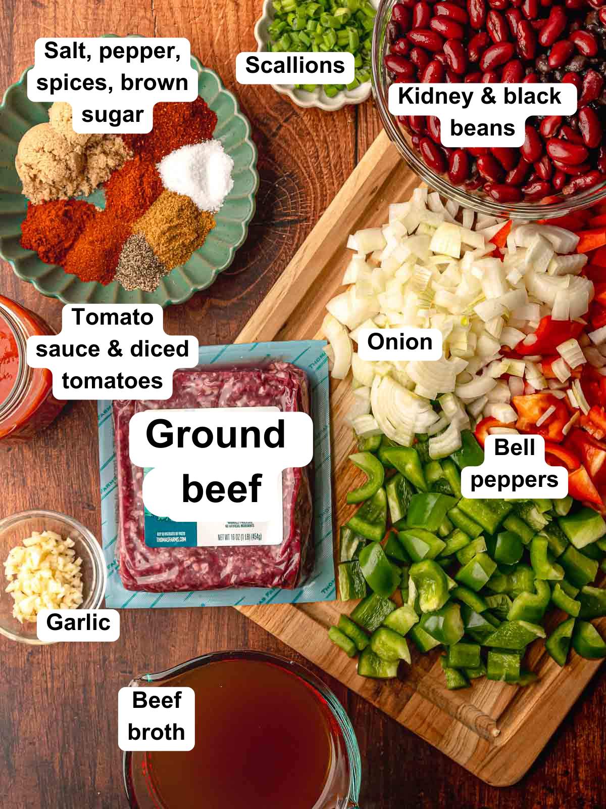 Overhead view of chili ingredients: ground beef, beans, diced onion, bell peppers, garlic, tomato sauce, beef broth, scallions, spices, and brown sugar.