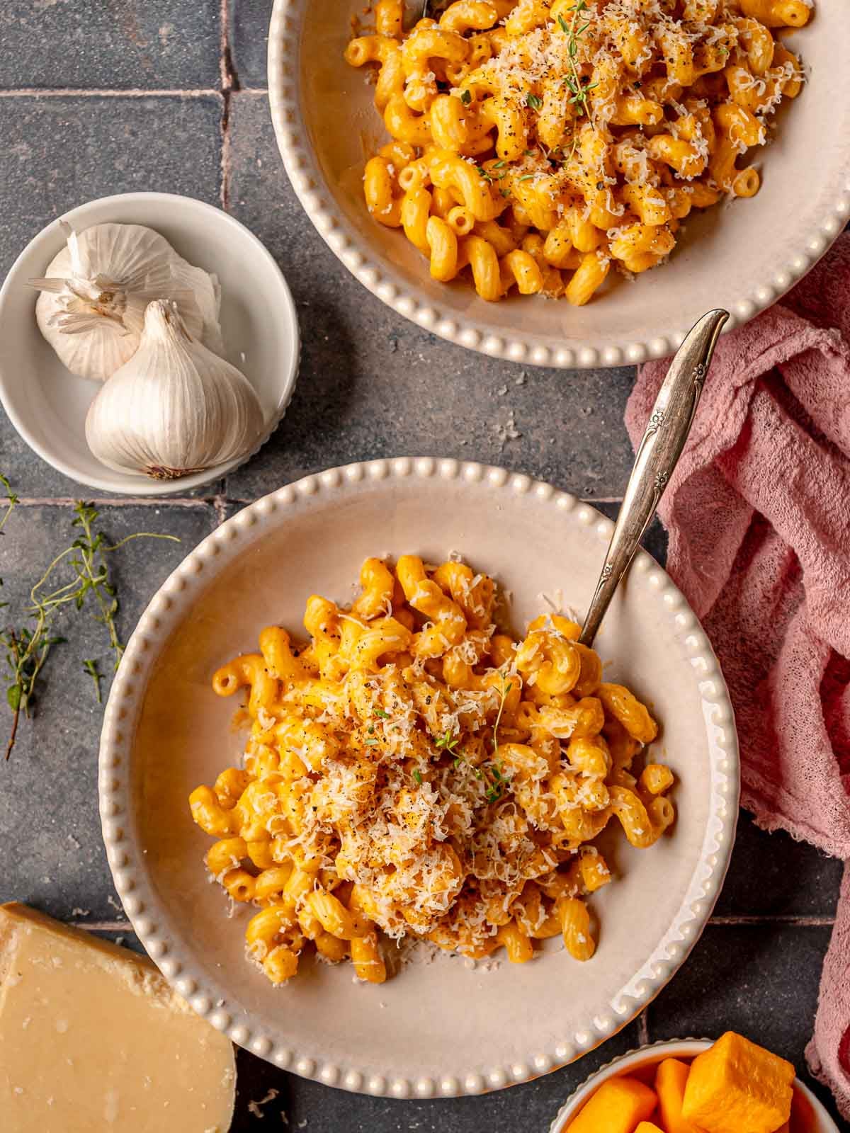 Bowls of butternut squash mac and cheese topped with grated cheese and herbs.