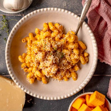Overhead view of butternut squash mac and cheese served in bowls with garlic and cheese on the side.