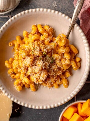 Overhead view of butternut squash mac and cheese served in bowls with garlic and cheese on the side.