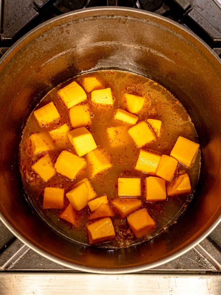 Cubes of butternut squash simmering in a pot with broth and spices.