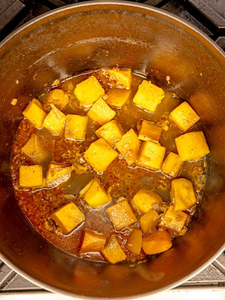 Cooked butternut squash softening in seasoned broth inside a pot.