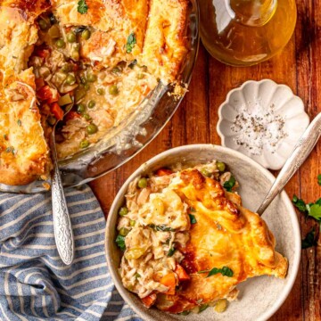Chicken pot pie with a serving scooped out and a bowl of pie beside it on a wooden table.